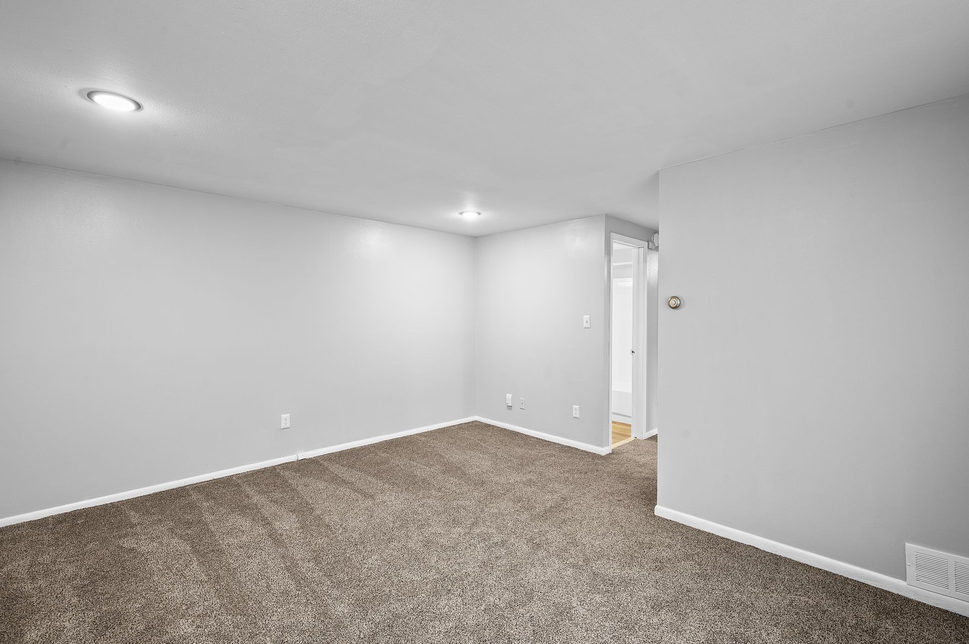 Empty room with gray walls, brown carpet, and recessed lighting.