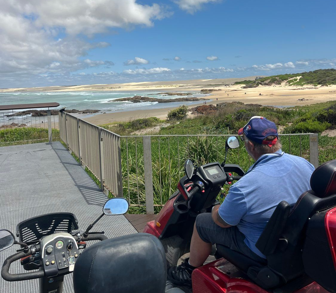 Person on mobility scooter overlooking a beach with blue sky and clouds.