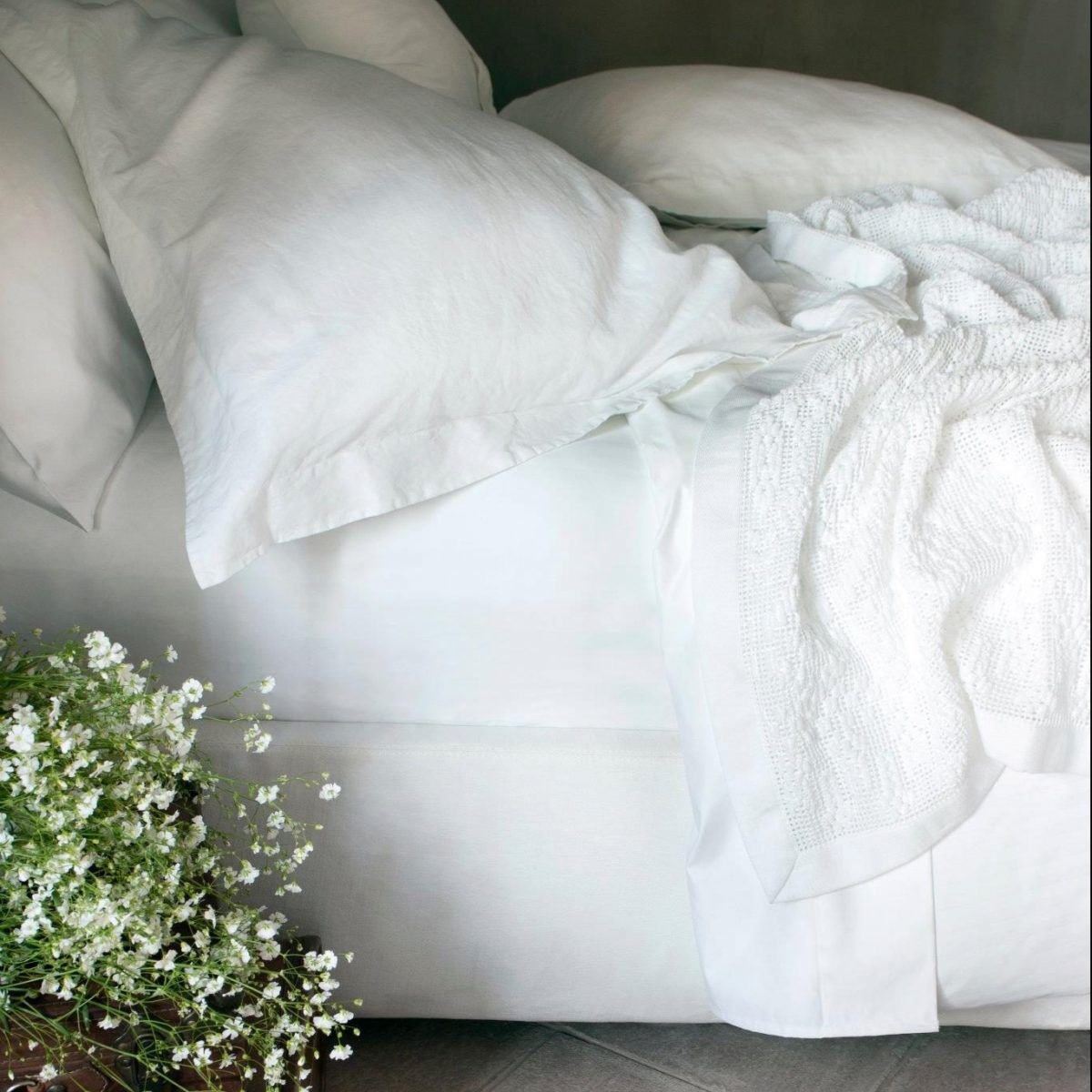 Una cama con sábanas blancas y almohadas junto a una cesta de gypsophila.