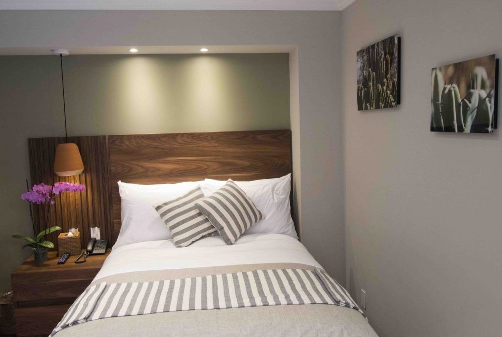 A bedroom with a bed , nightstand , and paintings on the wall.