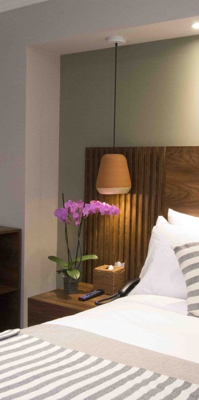 A hotel room with a bed , nightstand and lamp.