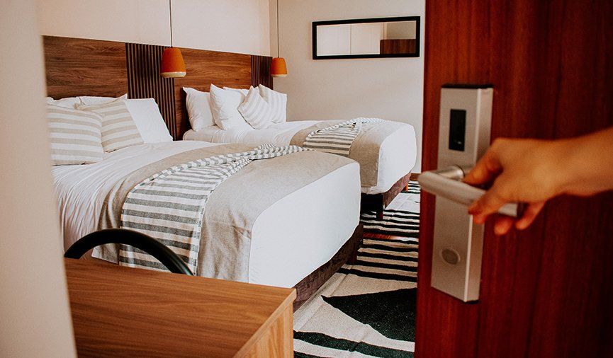 Una persona abre la puerta de una habitación de hotel con dos camas.