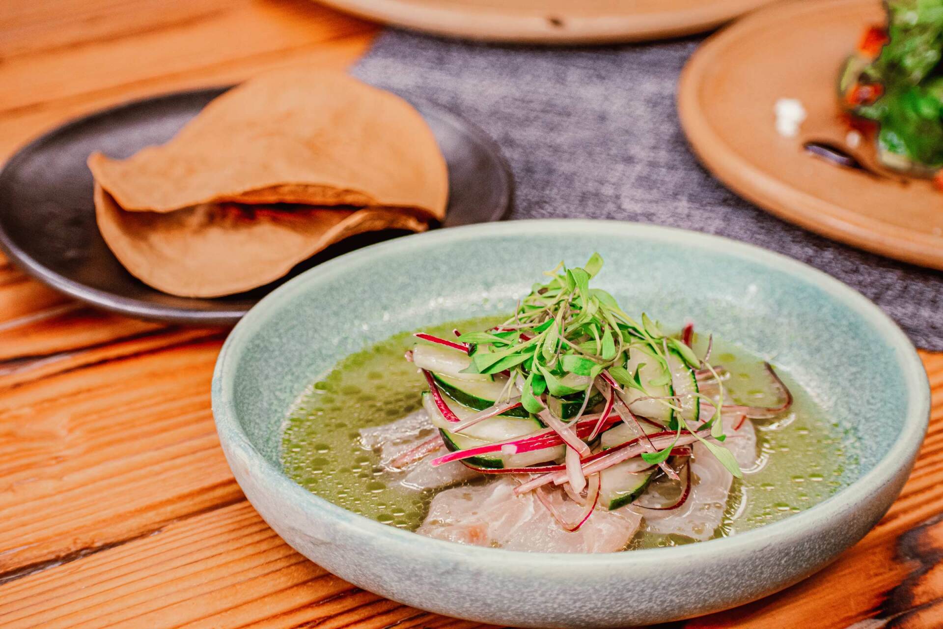 A bowl of food is sitting on a wooden table next to a plate of tortilla chips.