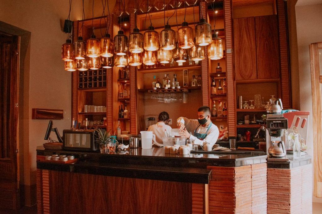 Un hombre que lleva una máscara está de pie detrás de una barra en un restaurante.