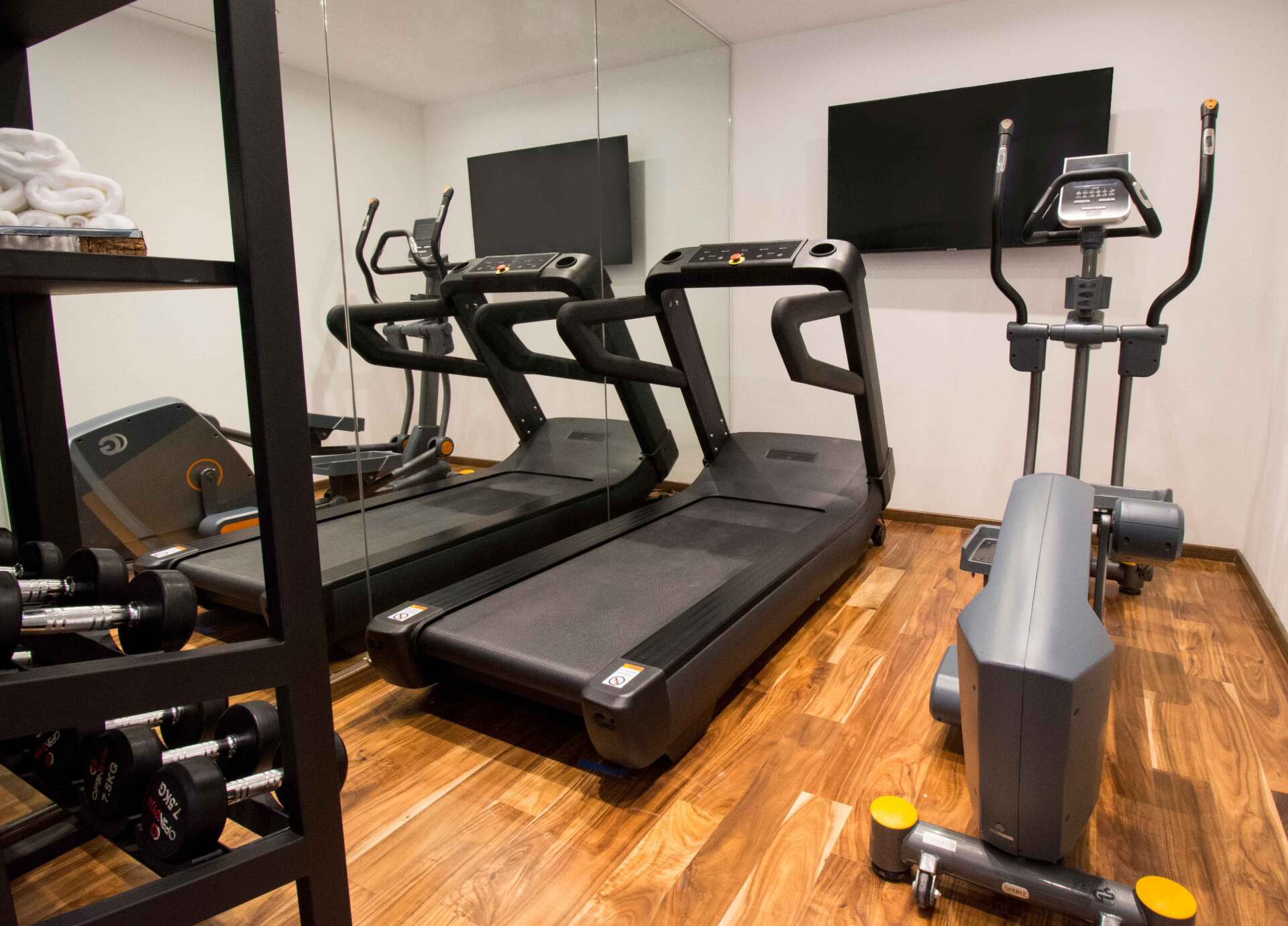 Un gimnasio con cintas de correr, elípticas, mancuernas y un televisor de pantalla plana.