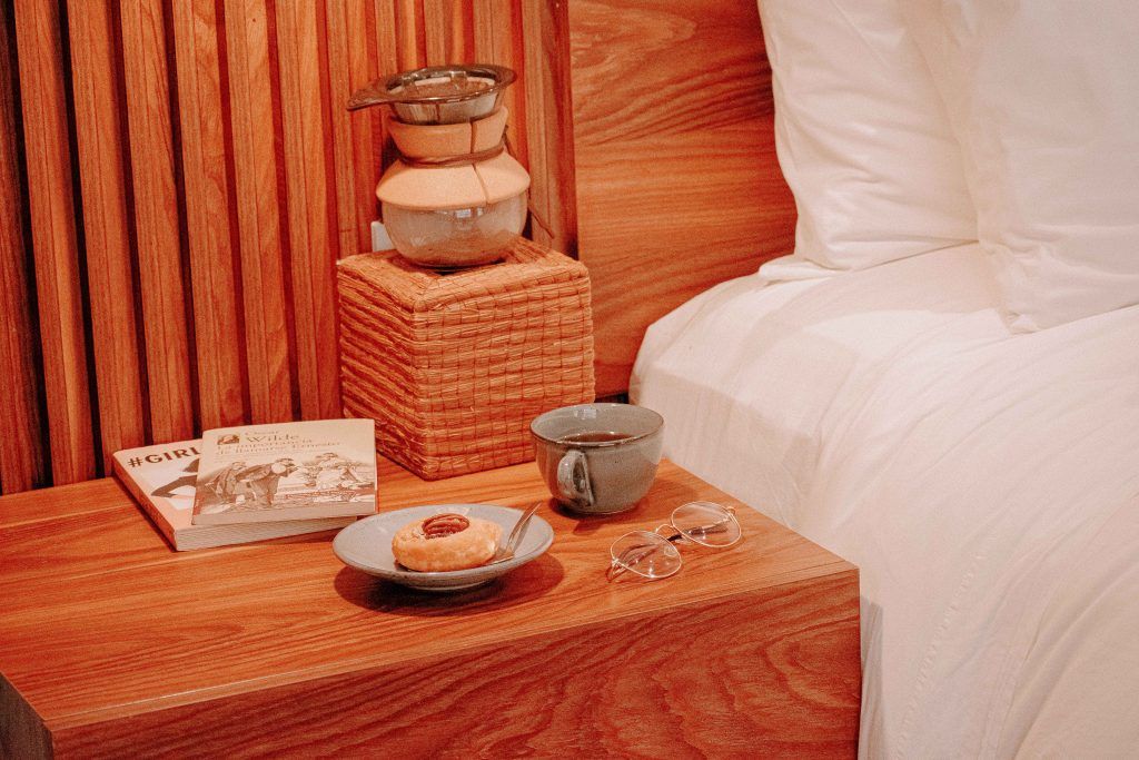 A wooden nightstand with a donut on it next to a bed.
