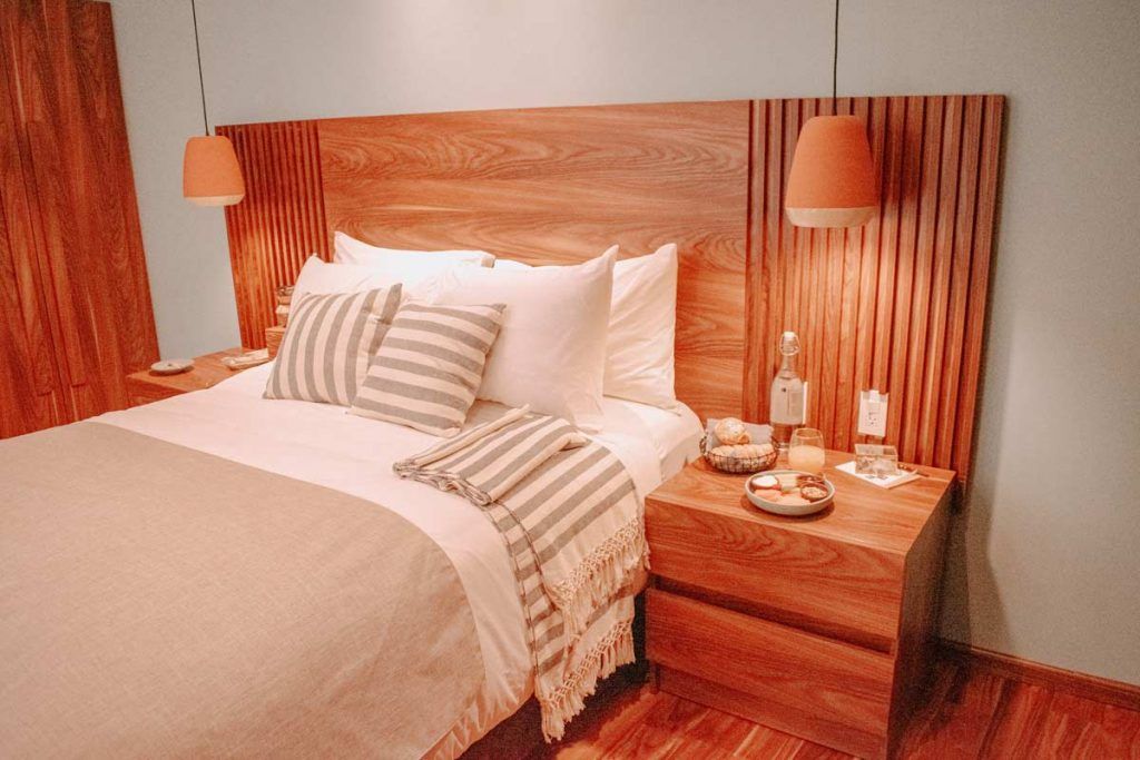 A bedroom with a bed , nightstand , lamps and a wooden headboard.