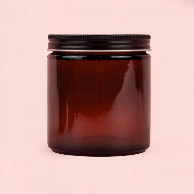 A brown glass jar with a black lid on a pink background.
