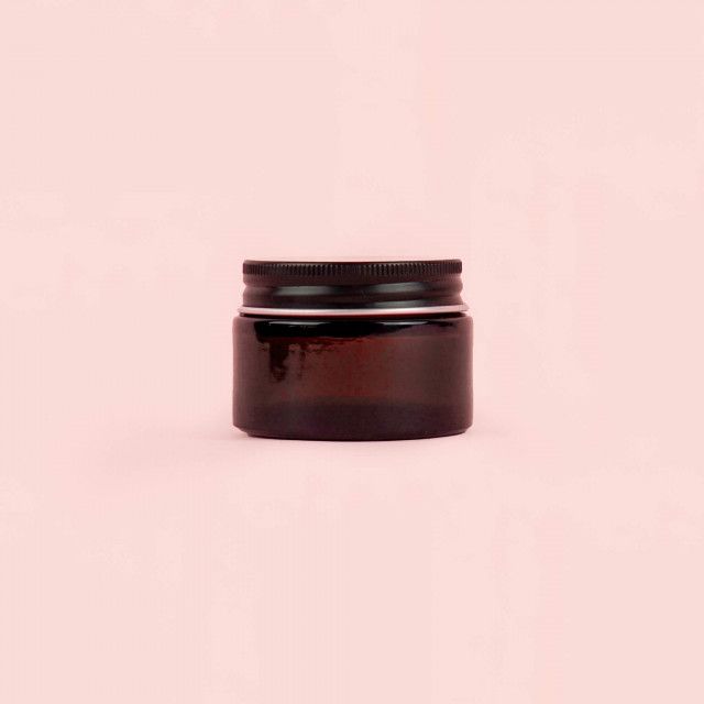 A brown glass jar with a black lid on a pink background.
