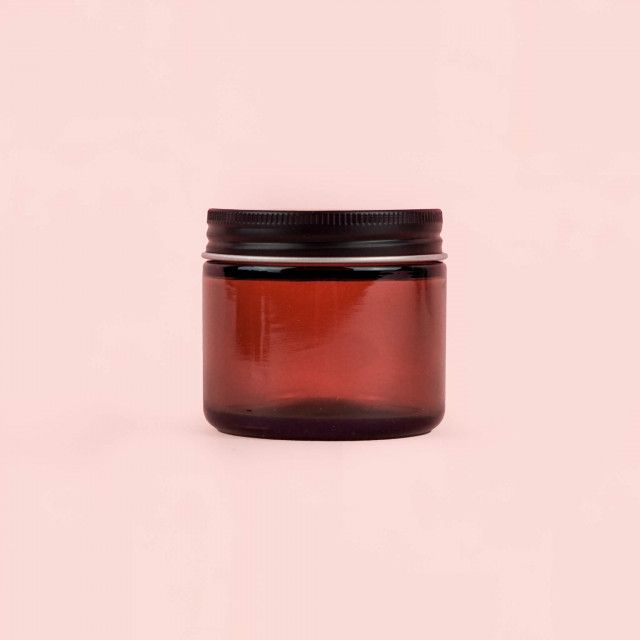 A brown glass jar with a black lid on a pink background.