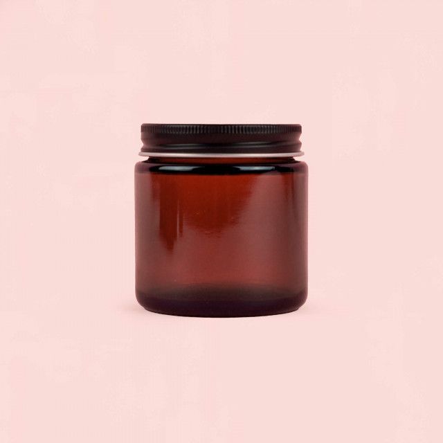 A brown glass jar with a black lid on a pink background.