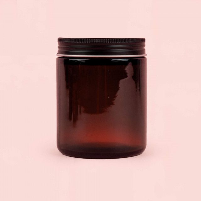 A brown glass jar with a black lid on a pink background.