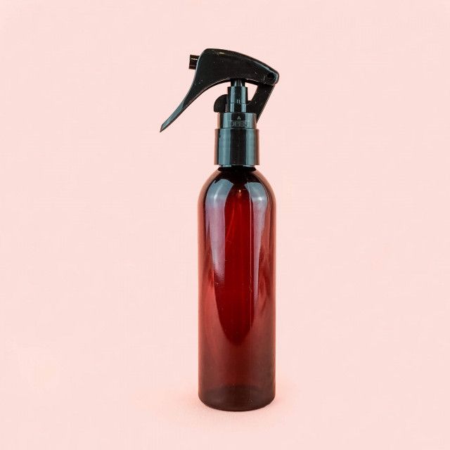 A red plastic spray bottle with a black sprayer on a pink background.
