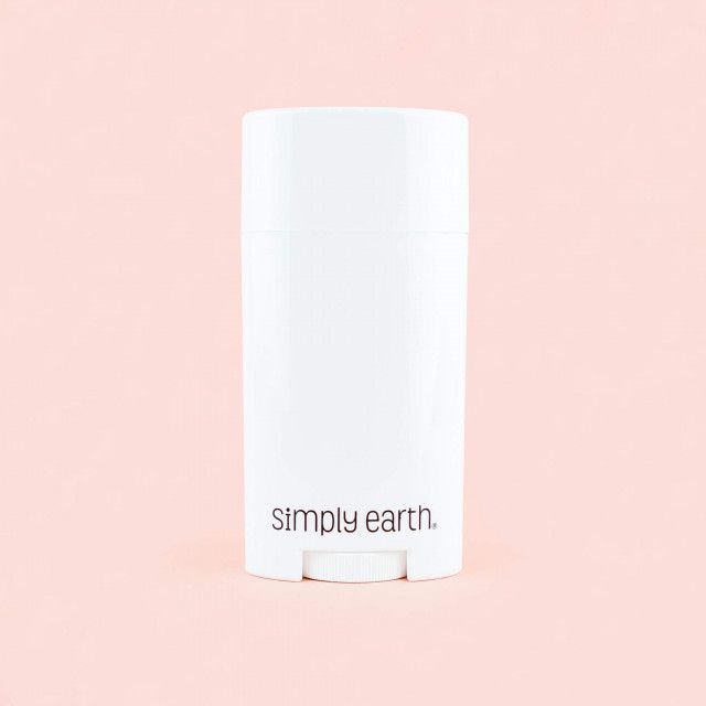 A white simply earth deodorant stick is sitting on a pink surface.