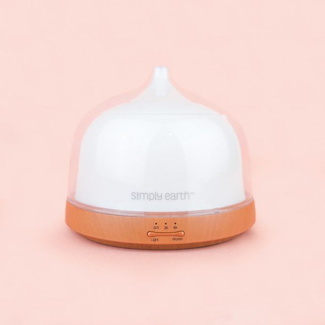 A simply earth essential oil diffuser is sitting on a pink surface.