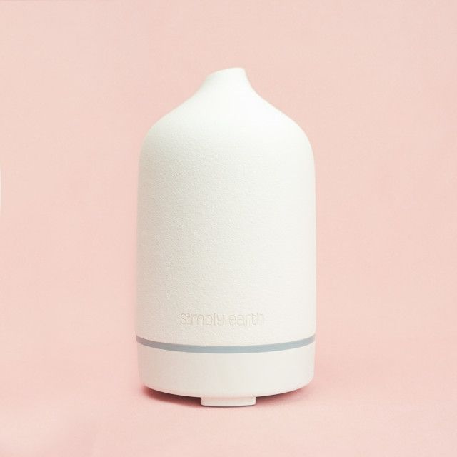 A white ceramic essential oil diffuser is sitting on a pink surface.