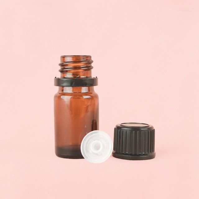 A small brown glass bottle with a white cap on a pink background.