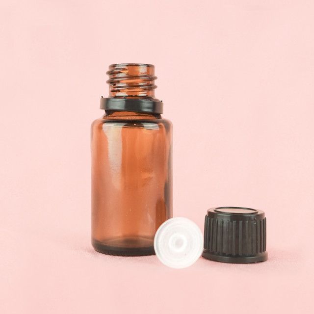 A brown glass bottle with a white cap on a pink background.
