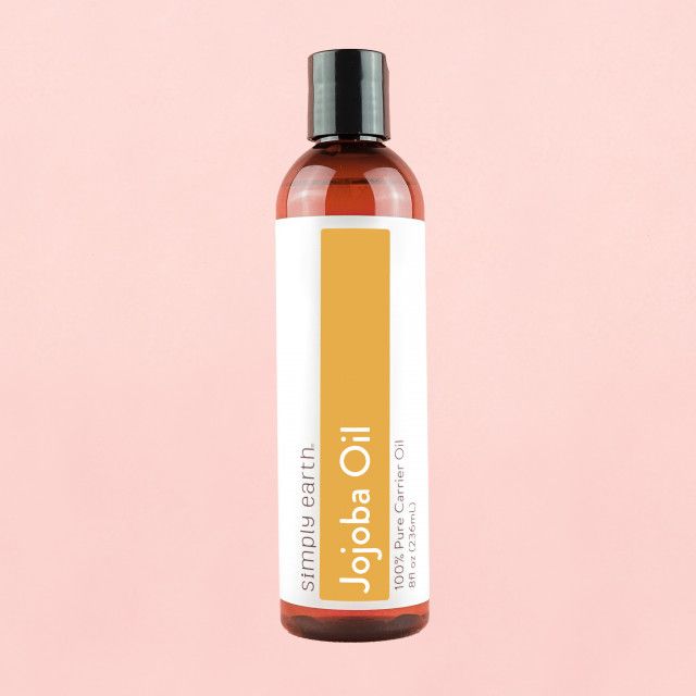 A bottle of jojoba oil on a pink background