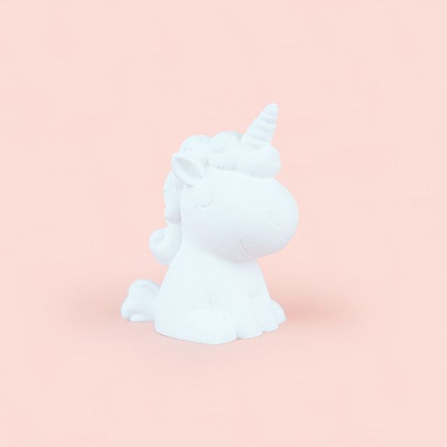 A white unicorn figurine is sitting on a pink surface.