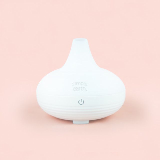 A white ultrasonic essential oil diffuser is sitting on a pink surface.