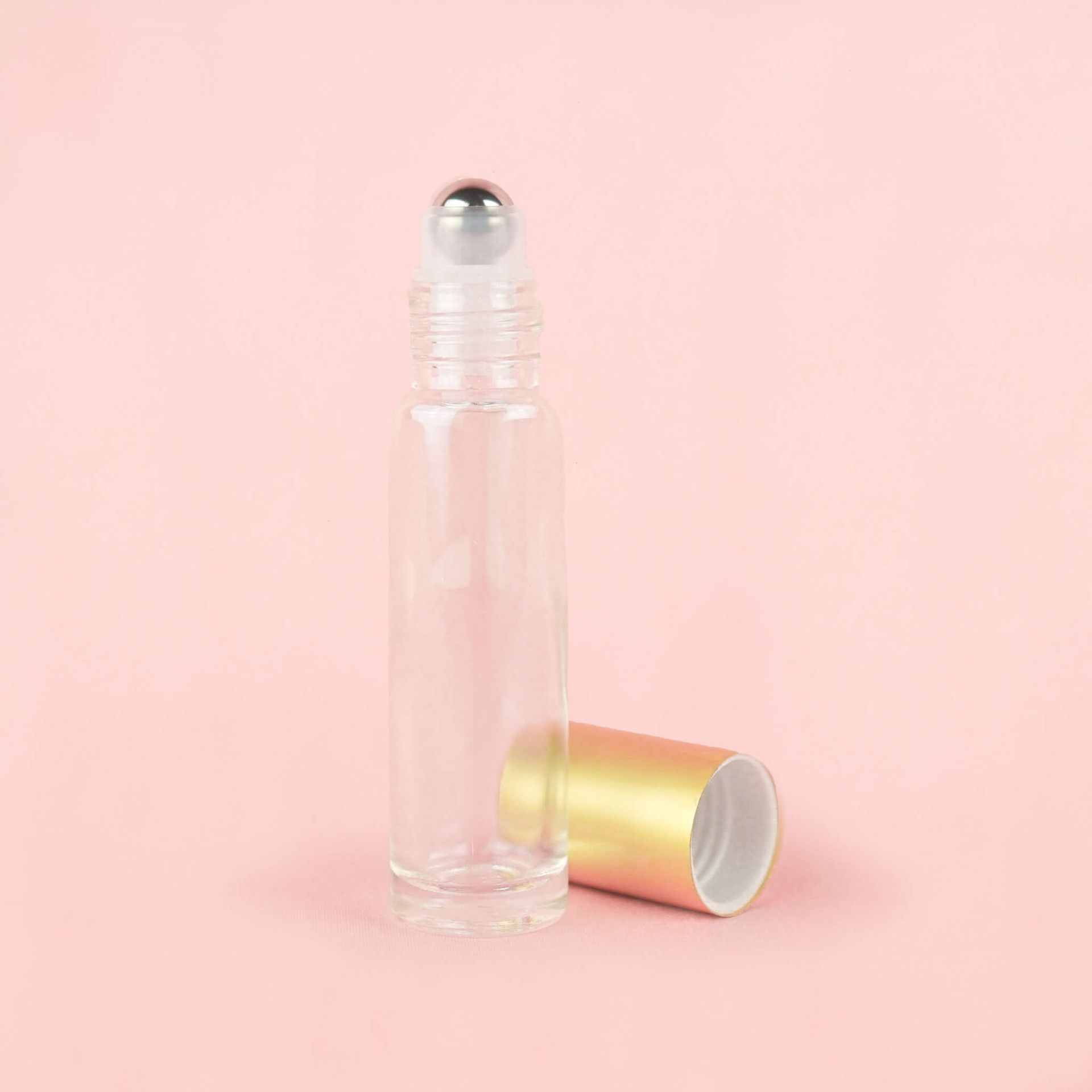 A row of clear glass roller bottles with gold caps on a pink background.