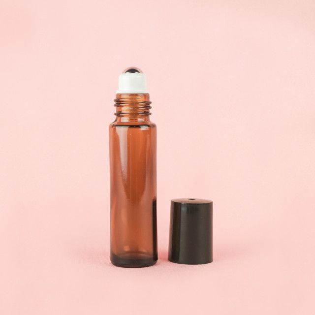 A brown glass roll on bottle with a black cap on a pink background.