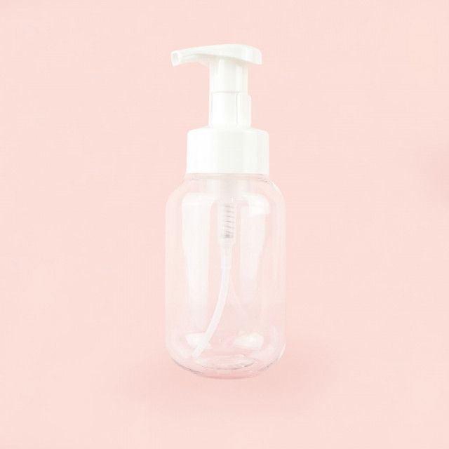 A clear plastic bottle with a white pump on a pink background.