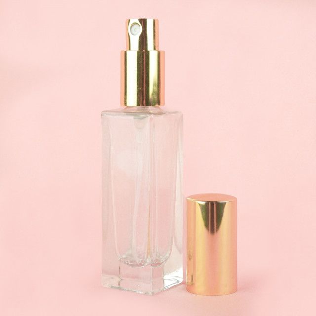 A clear perfume bottle with a gold sprayer on a pink background.
