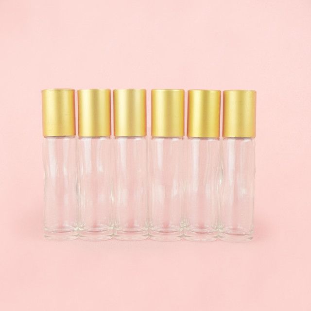A row of clear glass roller bottles with gold caps on a pink background.