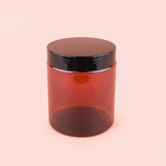 A brown plastic jar with a black lid on a pink background.