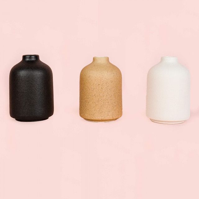 Three different colored vases are lined up on a pink background