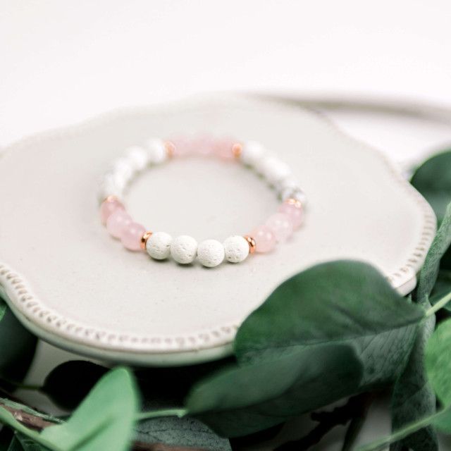 A bracelet with white beads and rose gold beads is sitting on a plate.
