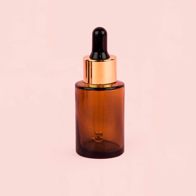 A brown glass bottle with a dropper on a pink background.