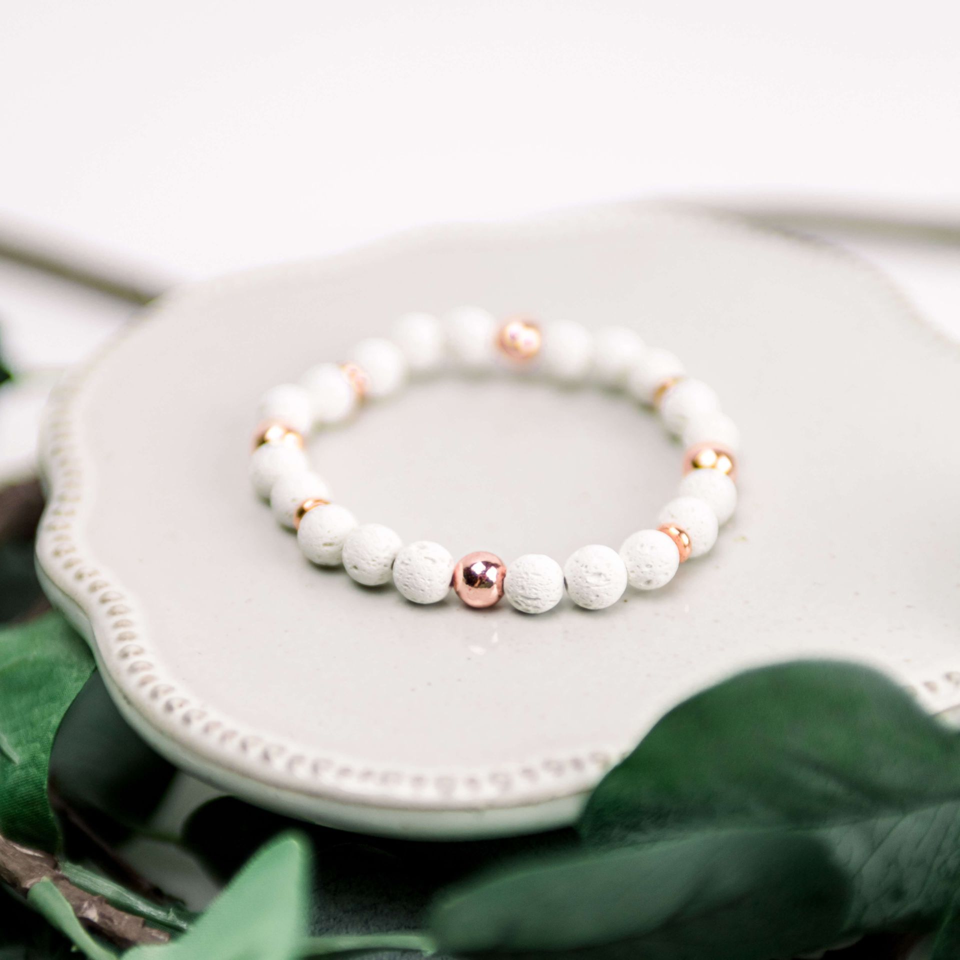 A bracelet with white beads and rose gold beads is sitting on a plate.