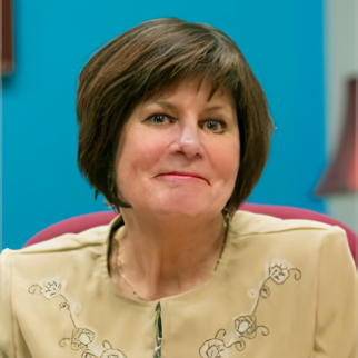 A woman wearing a white jacket and a necklace is smiling for the camera.