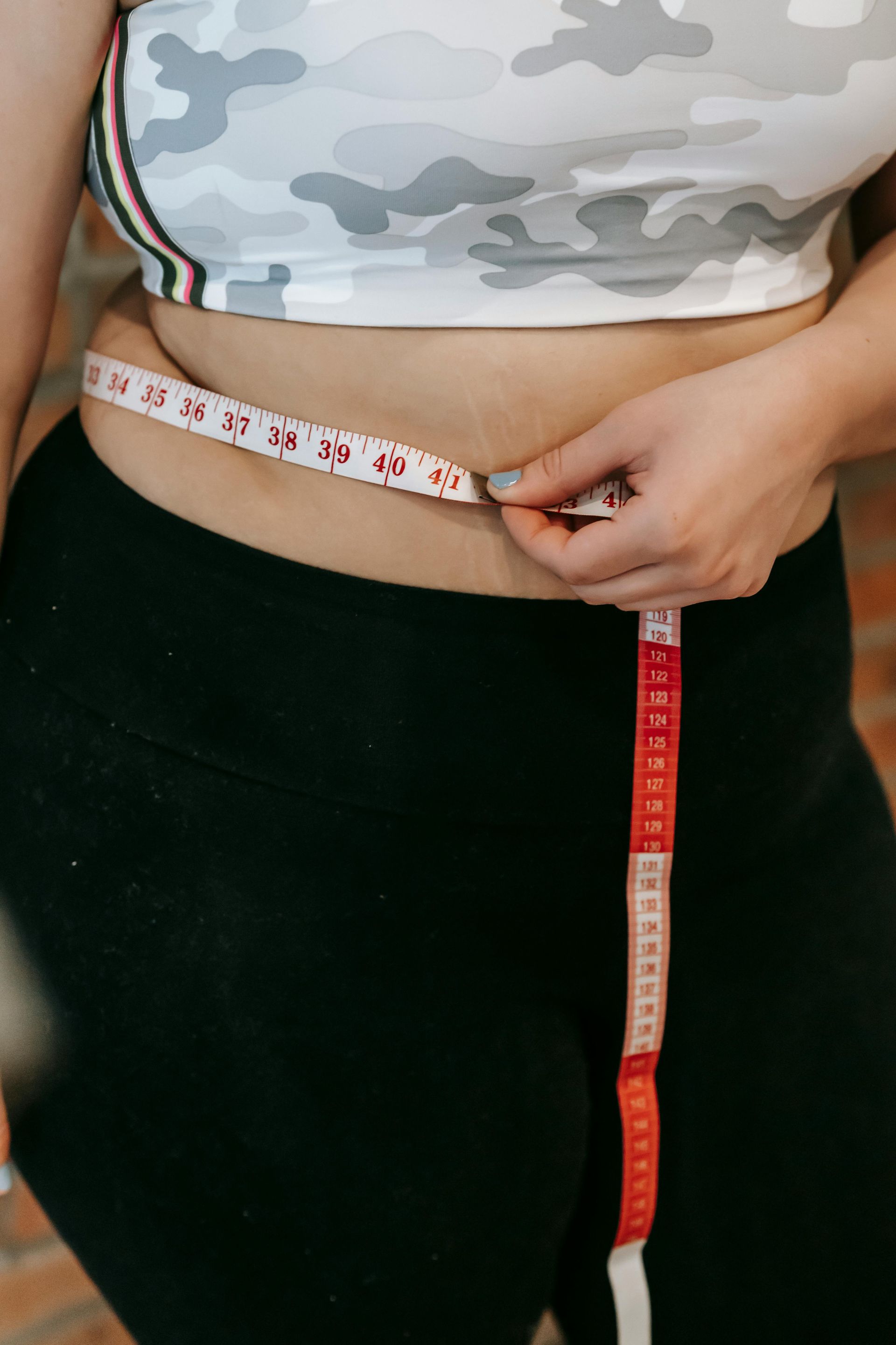 Woman in workout clothes measuring waist with a measuring tape.