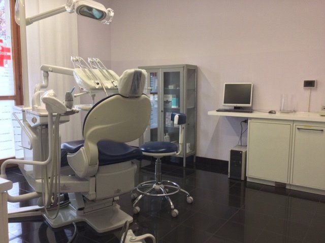 Sala per trattamenti odontoiatrici con poltrona reclinabile, lampada a soffitto e armadietti.