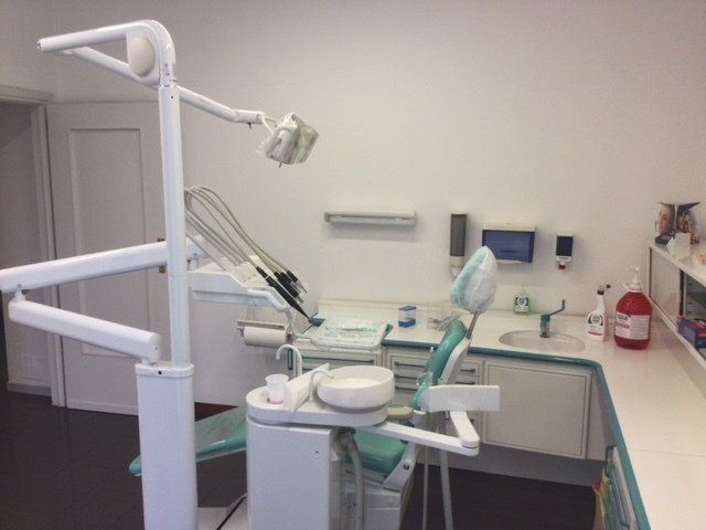 Studio dentistico con poltrona, lampada a soffitto, lavandino e armadietti in una stanza clinica pulita.