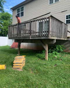 Person standing on a wooden backyard deck beside a house, with tools on the grass below.
