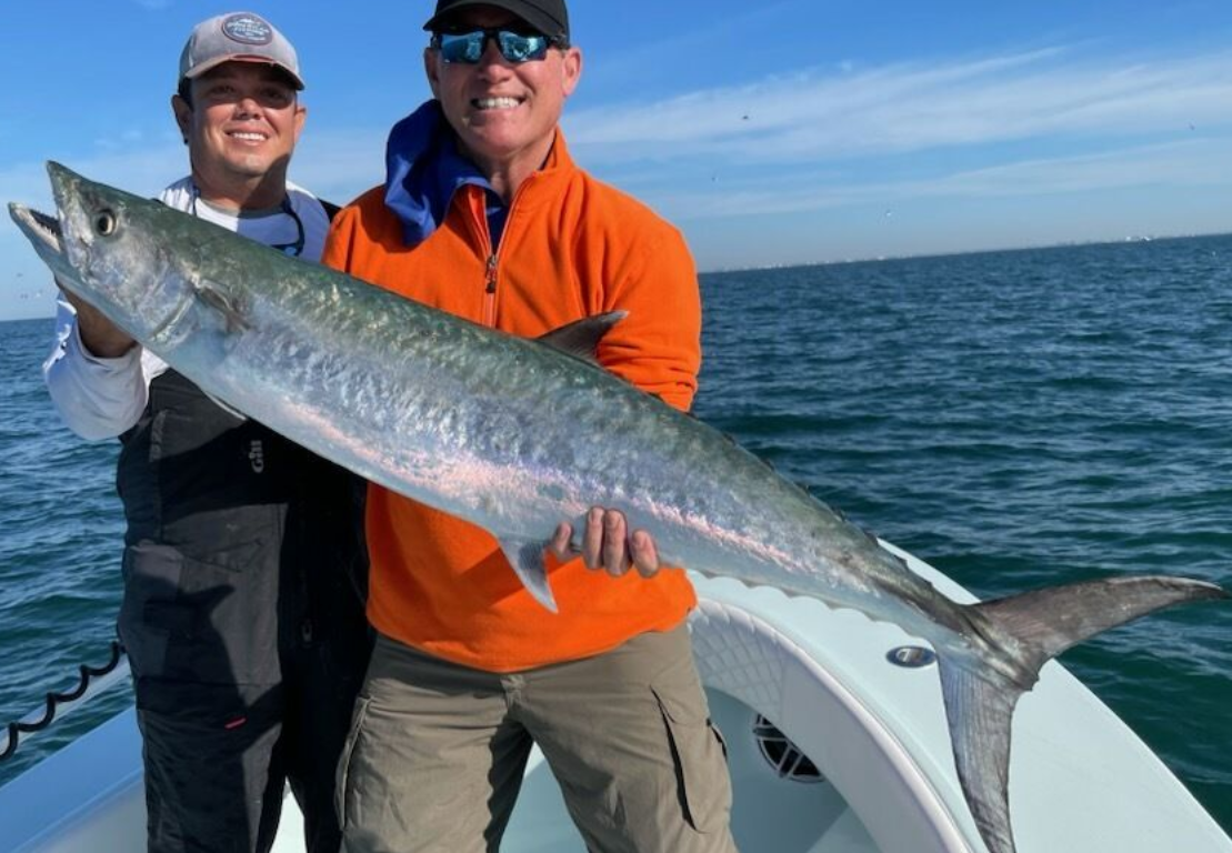 Two men are holding a large fish on a boat