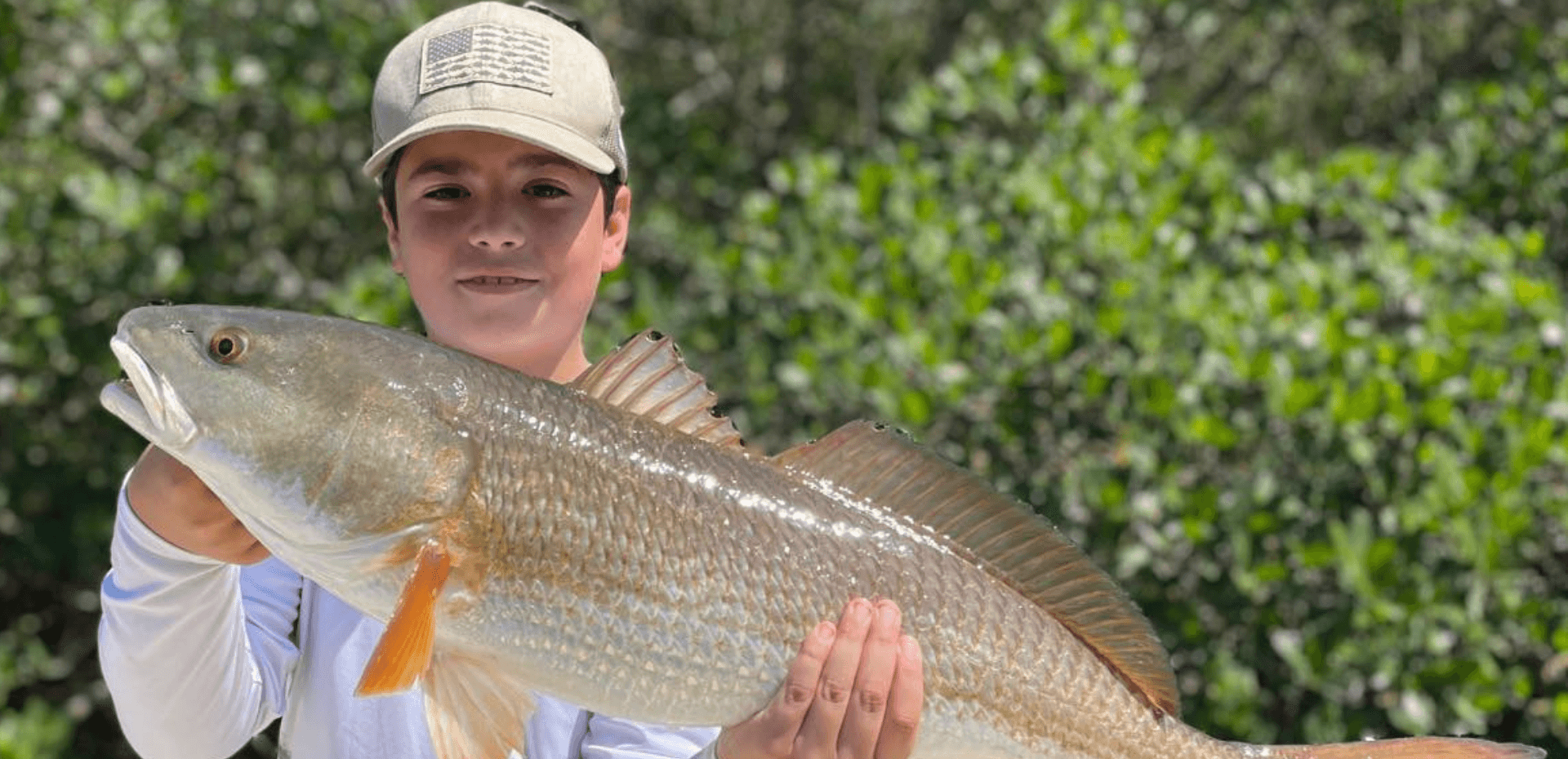 A young boy is holding a large fish in his hands.