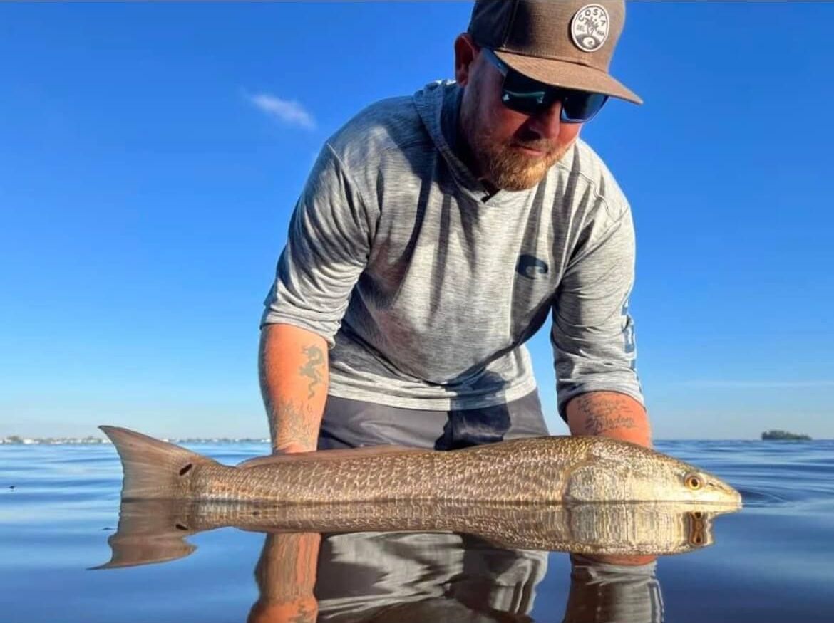 Captain William Wise is holding a large Redfish in the water.