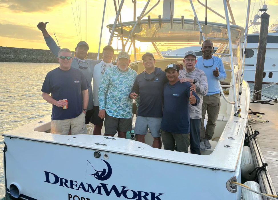 Group posing on a boat at sunset with a large yacht in the background