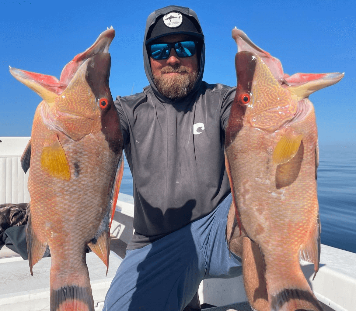 A man is holding two large fish on a boat