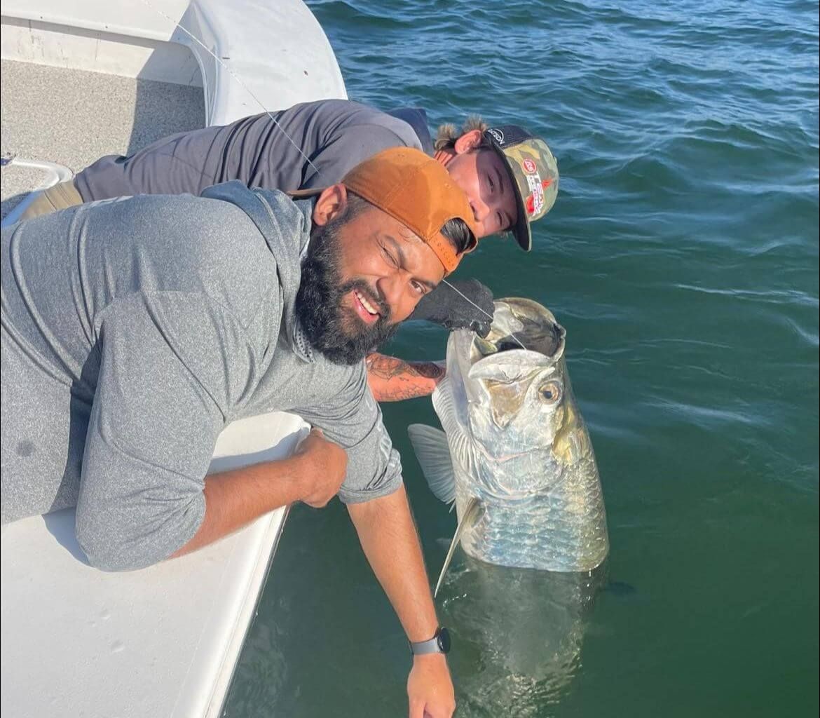 Two men are laying on a boat with a large fish in the water.