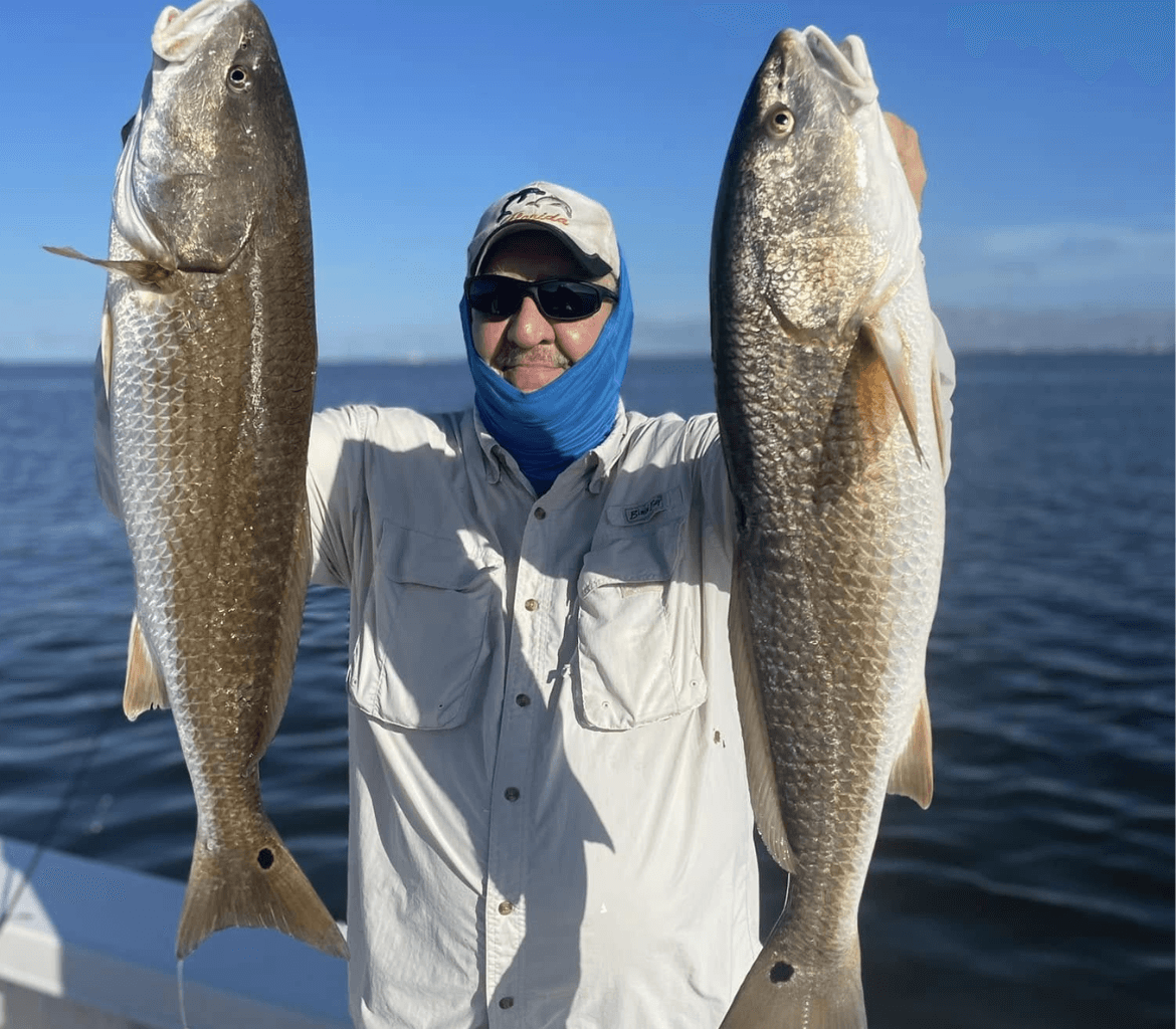 A man is holding two large fish in his hands