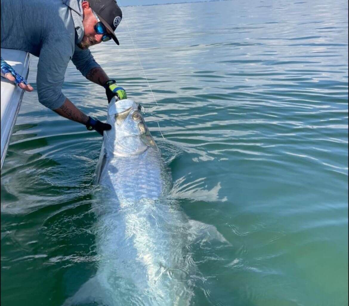 A man is holding a large fish in the water.