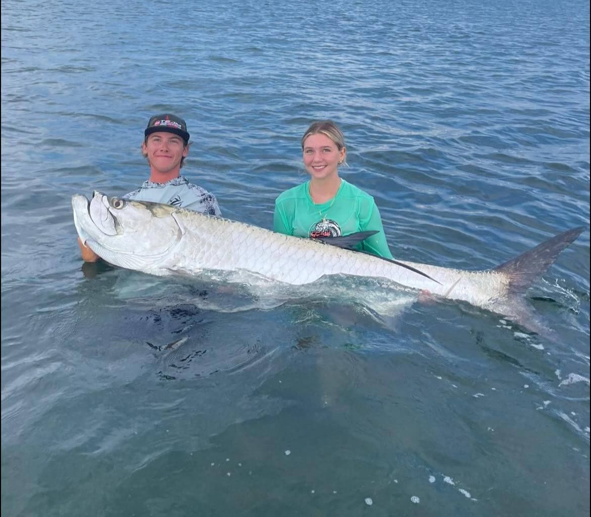 A man and a woman are holding a large fish in the water.