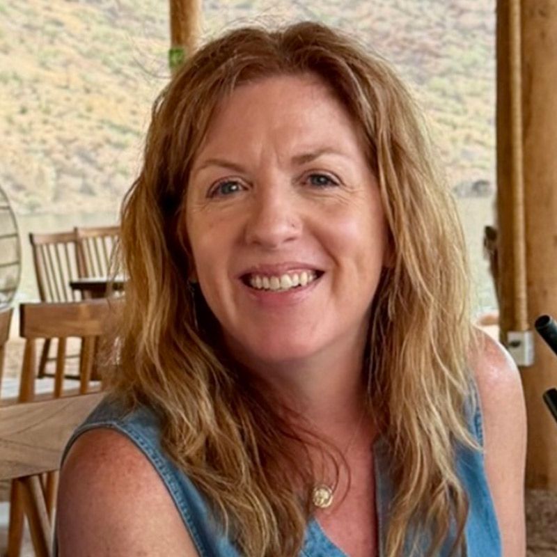 Smiling woman in a sleeveless blue top seated outdoors on a porch